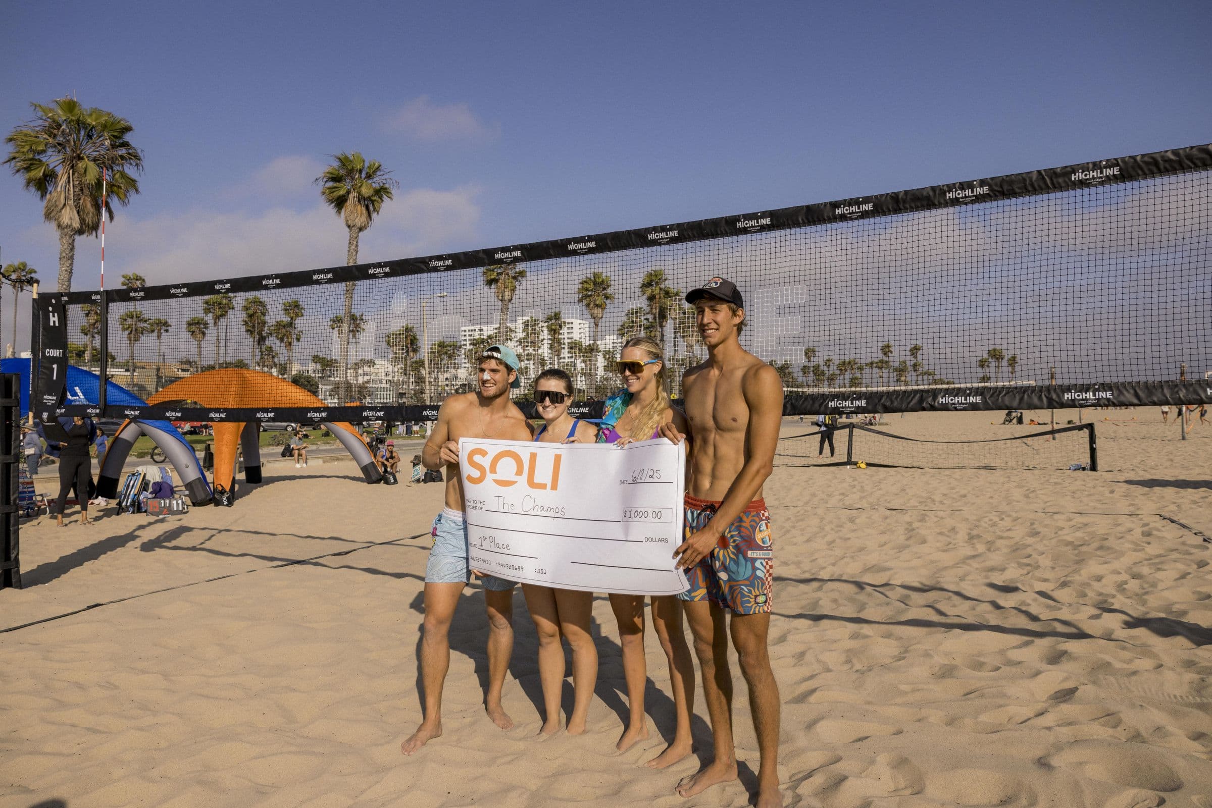 Winners holding an oversized Soli prize check on the sand