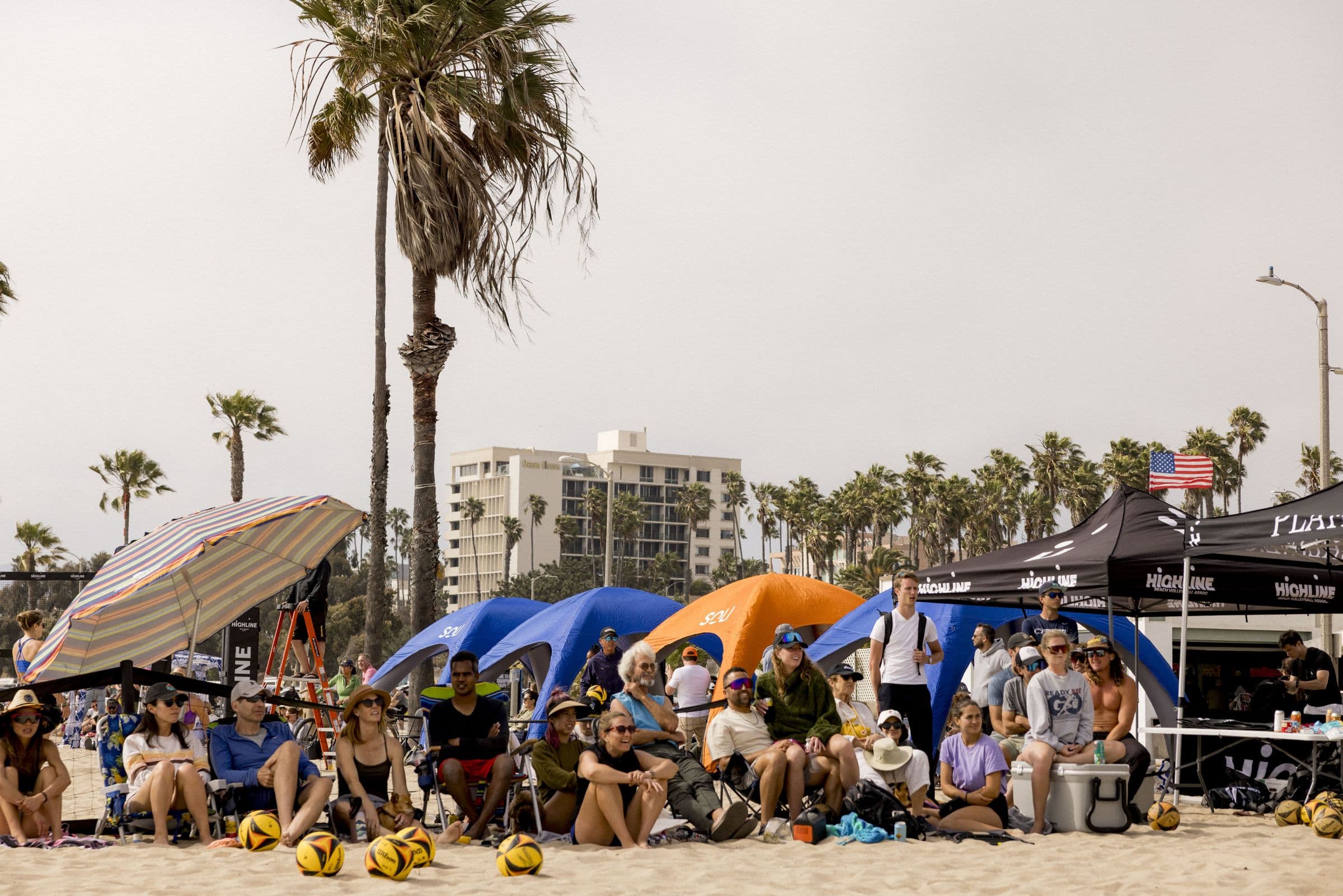 Fans packed under sponsor canopies and palm trees beside a Highline tournament court