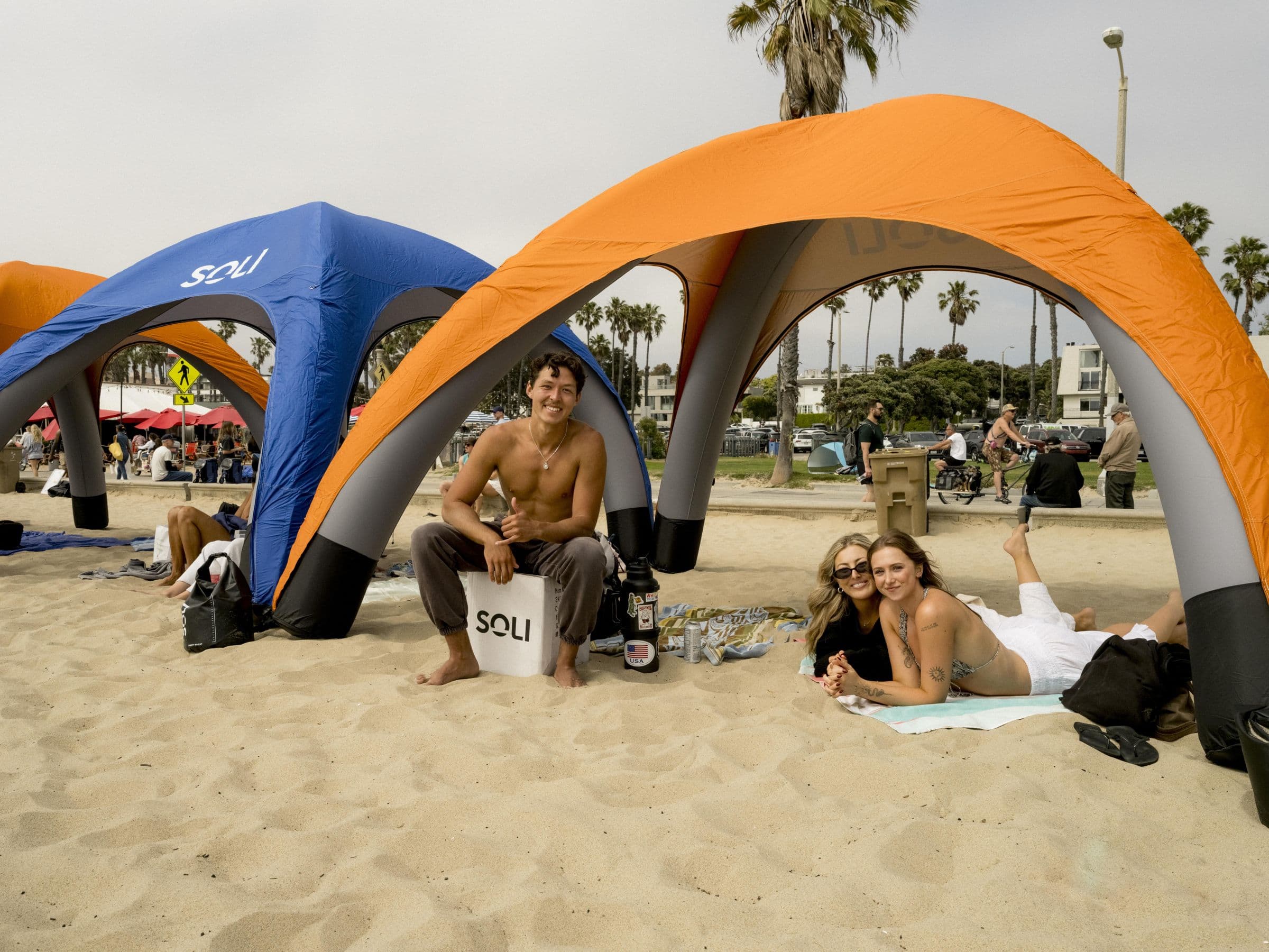 Players relaxing under orange and blue Soli canopies beside the courts